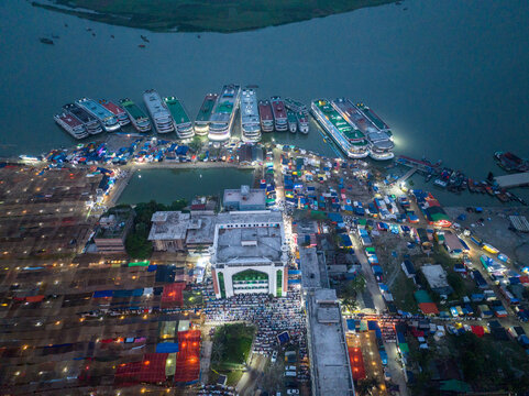 Aerial view of illuminated buildings and vibrant markets sprawling along the waterfront, where ferries dock under the twilight sky, Charmonai, Barisal Division, Bangladesh.