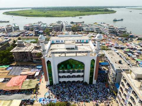 Aerial view of a grand mosque with striking white walls and green accents, surrounded by bustling markets and waterways, Charmonai, Barisal Division, Bangladesh.