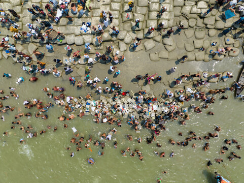 Aerial view of crowds gathering along the riverbank, their forms a mosaic against the textured stones and flowing water, Charmonai, Barisal Division, Bangladesh.