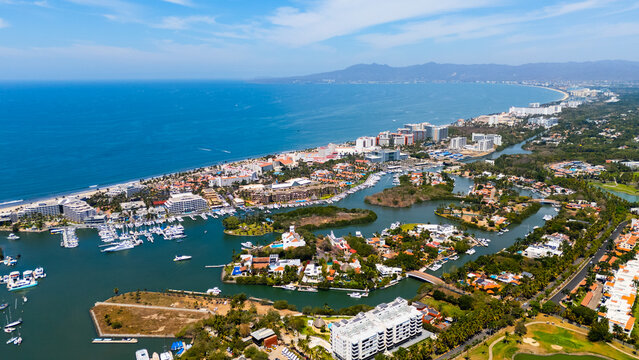 Aerial view of where the sapphire sea meets the sandy shore, cradling buildings and boats in a vibrant dance of blue and beige, Nuevo Vallarta, Mexico.