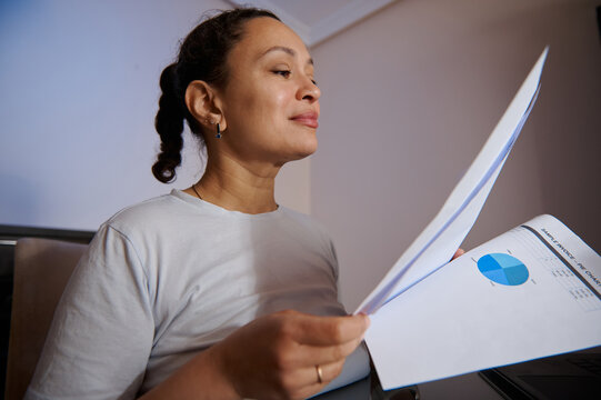 Businesswoman Reviewing Financial Report at Home Office Holding Printed Charts and Documents