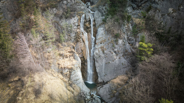 Aerial view of a cascading waterfall plunging into a pool of water surrounded by rocks and vegetation, Sallanches, Auvergne-Rhone-Alpes, France.