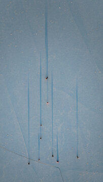 Aerial view of ice skaters on snow-covered frozen lake, their shadows stretching long and blue, Les Rousses, Bourgogne-Franche-Comte, France.