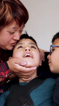 Happy latin american mother kissing her diverse children at home - Family love and disability care concept - Vertical video - ugc content