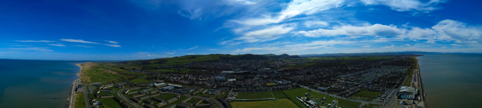 Aerial view of the coastal town nestled between the Irish Sea and rolling green hills under a vast, azure sky, Prestatyn, Wales, United Kingdom.