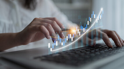 Fototapeta premium A focused individual types on a laptop, with a dynamic financial chart overlay representing growth and analysis in business and investment strategies. Impute