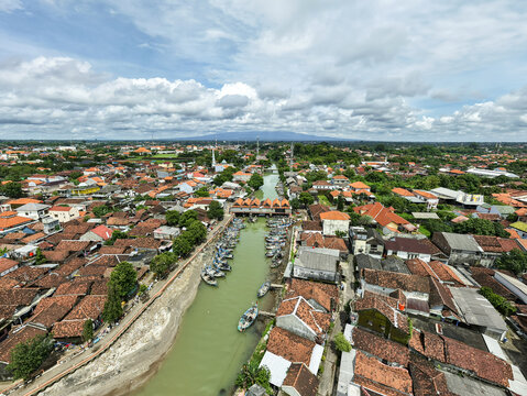 Aerial view of boats docked in a canal cutting through the heart of the city under a vast, cloudy sky, Jepara, Central Java, Indonesia.