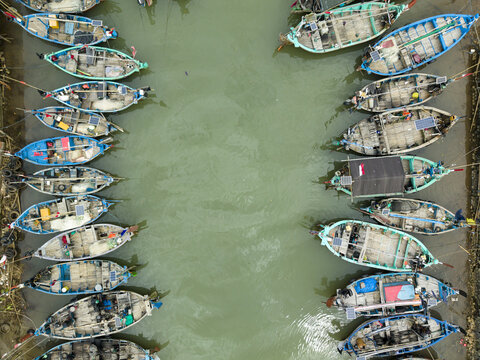 Aerial view of colorful boats clustered tightly in the Jepara Floating Fish Market, their vibrant hulls contrasting with the murky green water, Jepara, Central Java, Indonesia.