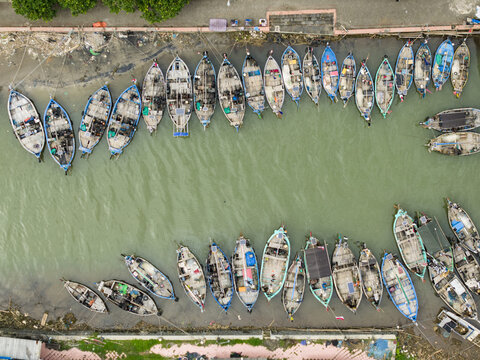 Aerial view of fishing boats docked in the harbor, their colorful hulls reflecting in the murky water, a tapestry of maritime life unfolds., Jepara, Central Java, Indonesia.