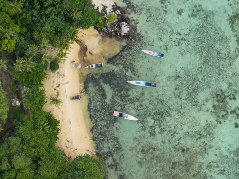 Aerial view of boats resting on the shore of Karina Beach where the turquoise water meets the lush green vegetation, Karimunjawa, Central Java, Indonesia.