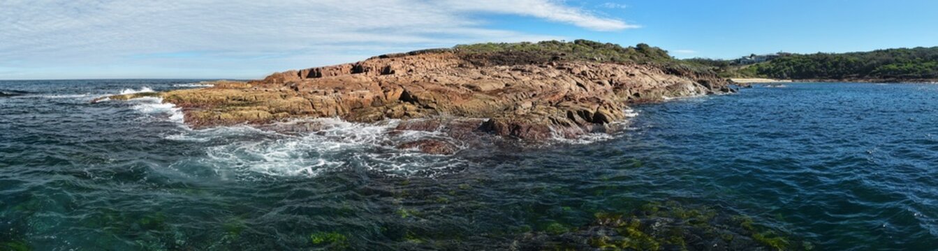 Aerial view of the rugged coastline where ochre cliffs meet the turquoise waters, creating a striking contrast of colors and textures, New South Wales, Australia.