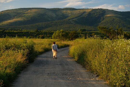 A woman from behind walks away to the summer mountain green landscape on a sunny day