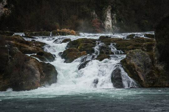 View of the powerful Rhine Falls cascading over moss-covered rocks, creating a dramatic display of nature's force, Neuhausen am Rheinfall, Switzerland.