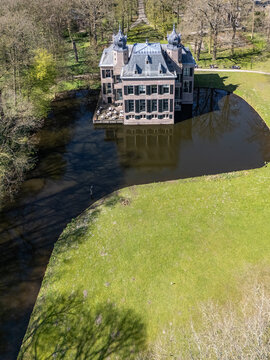 Aerial view of the historic Landgoed Oud Poelgeest castle reflected in the dark moat, surrounded by vibrant green grass and trees, Oegstgeest, Zuid-Holland, Netherlands.