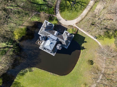 Aerial view of Landgoed Oud Poelgeest's castle reflecting in a dark moat, surrounded by pathways and green grass, Oegstgeest, Zuid-Holland, Netherlands.