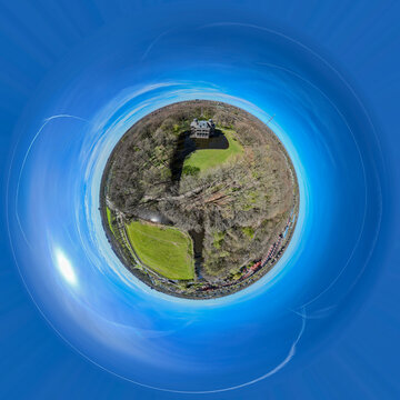 Aerial view of a lush landscape featuring vibrant green fields alongside dense woodlands, all under a swirling blue sky, Netherlands.