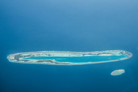 Aerial view of a tropical island surrounded by turquoise waters and fringed with white sand, a jewel amidst the deep blue sea, Flight from Male to Hanimaadhoo island, Maldives.