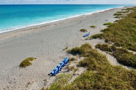 Aerial view of turquoise waters meet the sandy shore of Jupiter Island, with blue chairs dotting the landscape, Jupiter Island, Florida, United States.