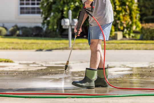 Man using pressure washer to power wash residential concrete driveway sidewalk.