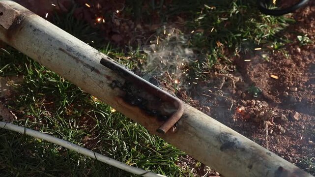 A welder is performing arc welding on an iron pipe in an open area.