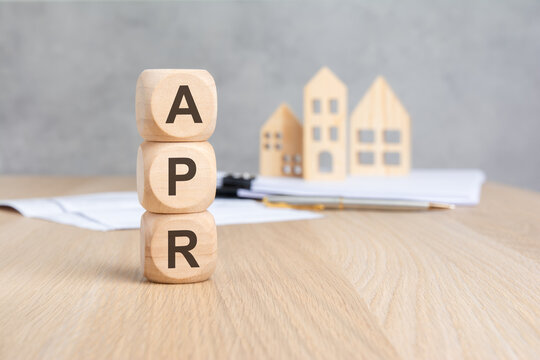 APR - Annual Percentage Rate - acronym on wooden blocks. Blurred background with miniature houses and documents. Mortgage loan concept.