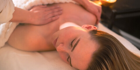 Fototapeta premium Facial massage session in cozy spa, esthetician caring for relaxed woman on treatment bed, skincare wellness ritual, aromatherapy candlelight, self care, mirror reflection.