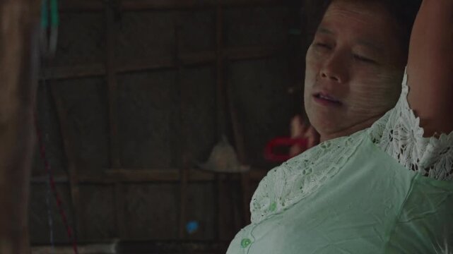 Southeast asian woman with traditional thanaka paste combing her long black hair in a rural village