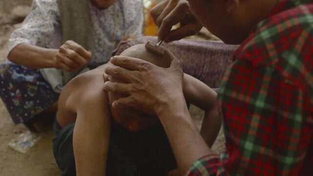 Man carefully shaves a young child's head with a straight razor during a traditional ceremony