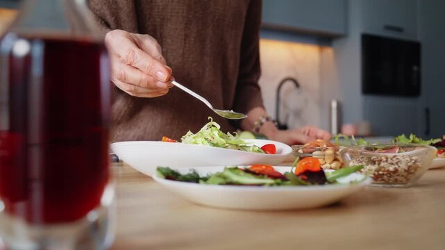 Mature woman hand adds seeds to fresh salad on wooden table