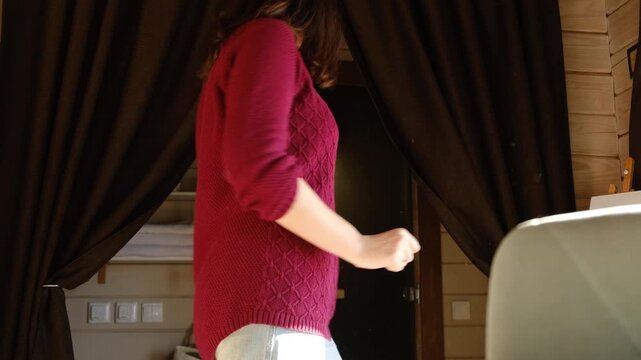 Relaxed woman enjoying by dining room. Casual morning cheerful woman dancing. Girl in bright kitchen singing playful stretches. Young adult female twirls, grooves. Lady moves to music, feels overjoyed