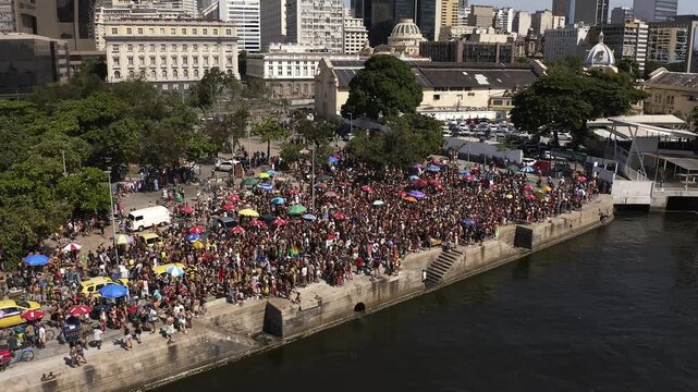 Aerial View, Drone Footage of big and crowded carnival block parade in downtown Rio de Janeiro in Brazil.  Drone Shot in Orbit mode with buildings background on the edge of Guanabara Bay.