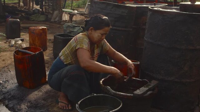 Woman in Myanmar extracting crude oil by hand from a rag in an artisanal oil field