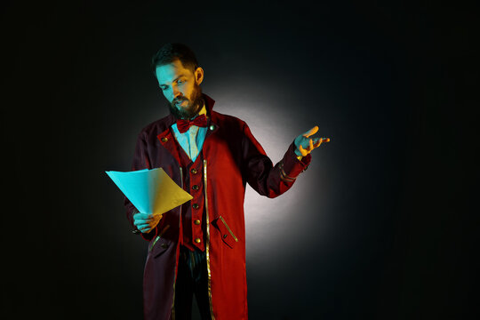 Professional actor in suit with script performing on black background with spotlight