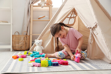 Little girl playing with building blocks near toy wigwam in playroom © New Africa