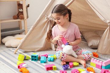 Little girl playing with building blocks near toy wigwam in playroom © New Africa