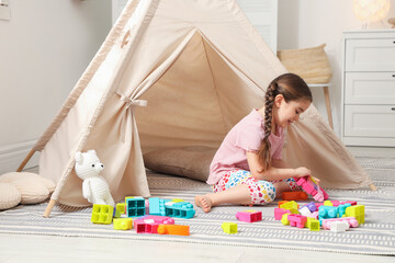 Little girl playing with building blocks near toy wigwam in playroom © New Africa