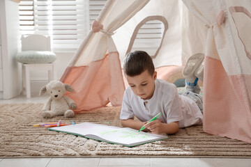 Little boy drawing in sketchbook near toy wigwam at home © New Africa
