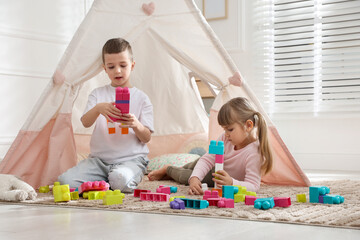Little kids playing with building blocks near toy wigwam at home © New Africa