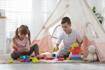 Little kids playing with building blocks near toy wigwam at home © New Africa