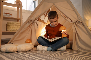 Little boy reading book in toy wigwam at home © New Africa