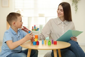 Professional psychologist working while little boy with toys at wooden table indoors