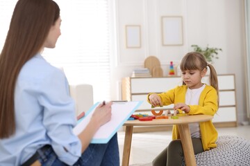 Professional psychologist working while little girl playing with toys at wooden table indoors