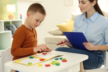 Professional psychologist working while little boy playing with toys at white table indoors