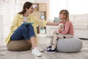 Professional psychologist working with little girl on poufs indoors