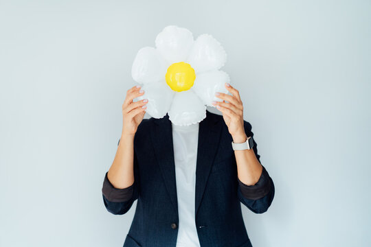 Business woman hides head behind large daisy flower balloon, symbolizing positivity and optimism in business. Concept of cheerful brand image and power of presenting simplicity, growth, fresh ideas.