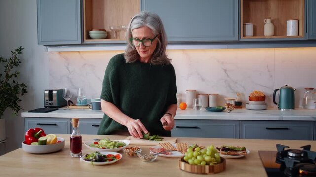 Grey-haired woman slices cucumber cooking at island counter