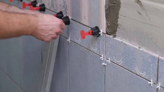 Worker Laying Ceramic Tiles on the Wall. Repairman Placing White Gray Square Tiles, Applying Adhesive. Builder Installing Tile Using Leveler, Tile Leveling Clips. Tiling. Finishing Repair Work. 4K
