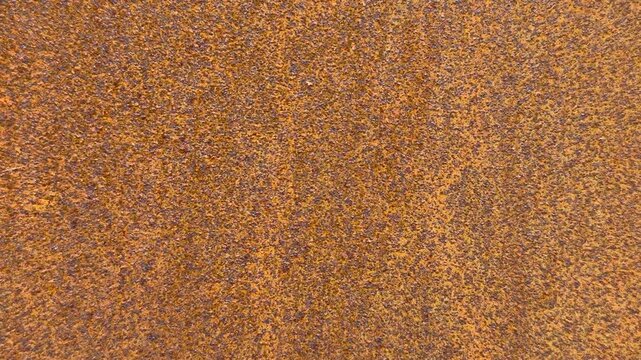 Close-up rusty steel sheet texture, granular orange-brown patina with heavy corrosion and flaking, rough grain and speckled surface.