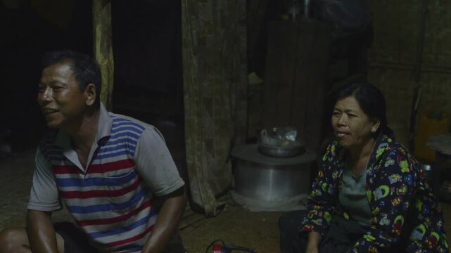 Rural asian man and woman watching something with changing emotions in a poor wooden home in Myanmar