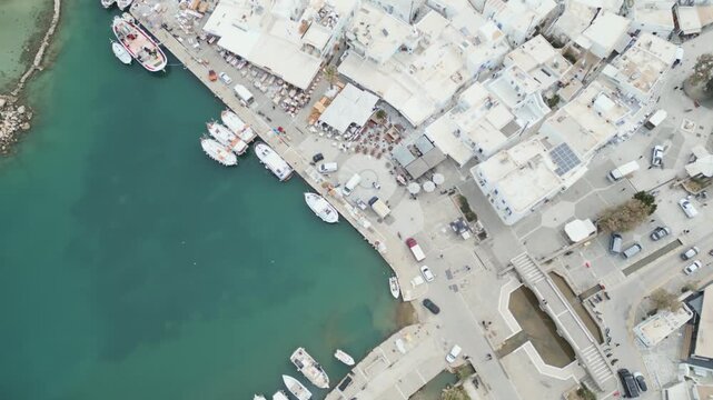 Aerial drone view of Naousa village on Paros island, Greece, showing traditional white buildings, coastal harbor and clear blue sea in daylight. Ideal for travel, tourism and Mediterranean lifestyle 